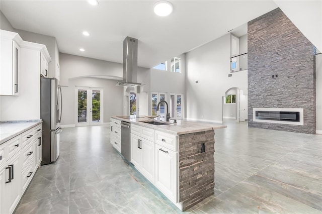 kitchen featuring island range hood, arched walkways, stainless steel appliances, french doors, and a sink