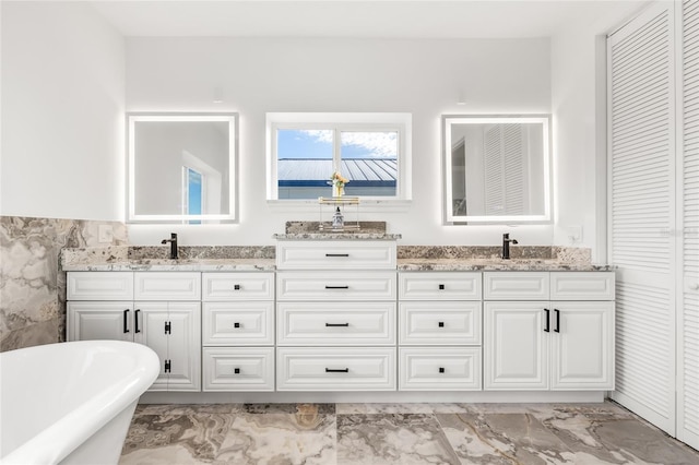 full bath with double vanity, marble finish floor, a sink, and a soaking tub