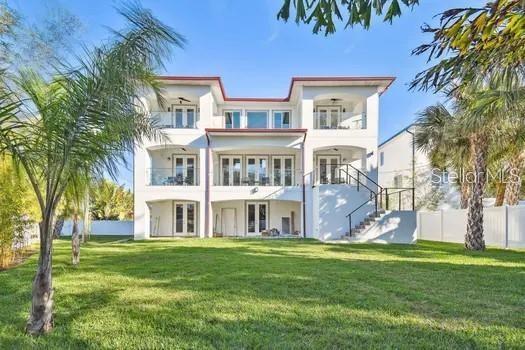 rear view of property featuring a lawn, a balcony, stairs, fence, and french doors