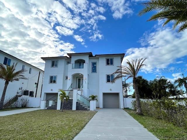 view of front of property featuring driveway, an attached garage, fence, a front lawn, and stucco siding