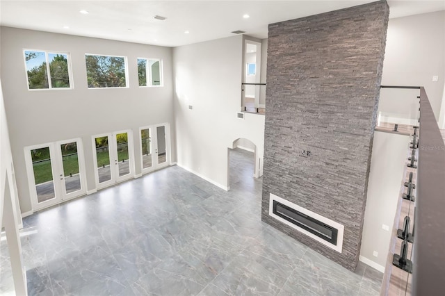 unfurnished living room with a stone fireplace, recessed lighting, a high ceiling, baseboards, and french doors