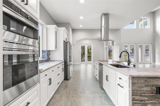 kitchen featuring arched walkways, island range hood, stainless steel appliances, a sink, and french doors