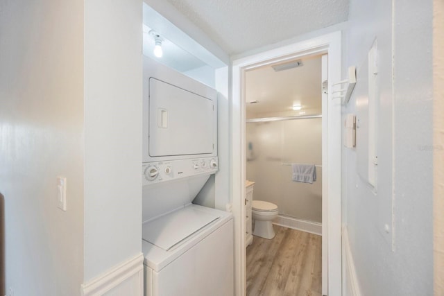 bathroom with stacked washer / dryer, hardwood / wood-style flooring, vanity, toilet, and a textured ceiling