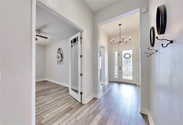 foyer with ceiling fan with notable chandelier and light hardwood / wood-style flooring