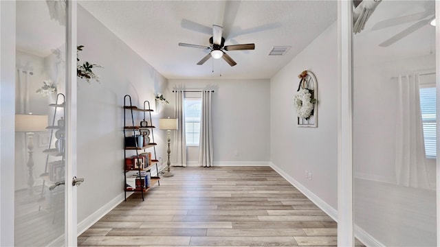 living area with ceiling fan, a textured ceiling, and light wood-type flooring