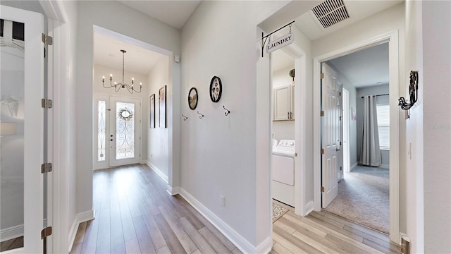 hall featuring washing machine and dryer, a notable chandelier, light hardwood / wood-style floors, and a healthy amount of sunlight