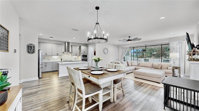 dining room with sink, ceiling fan with notable chandelier, and light hardwood / wood-style floors