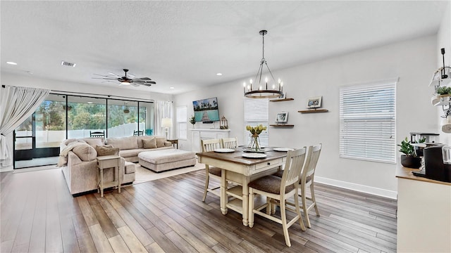 dining space with hardwood / wood-style flooring, ceiling fan with notable chandelier, and a textured ceiling