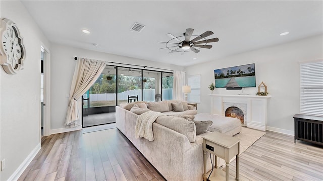 living room with ceiling fan, a fireplace, and light wood-type flooring