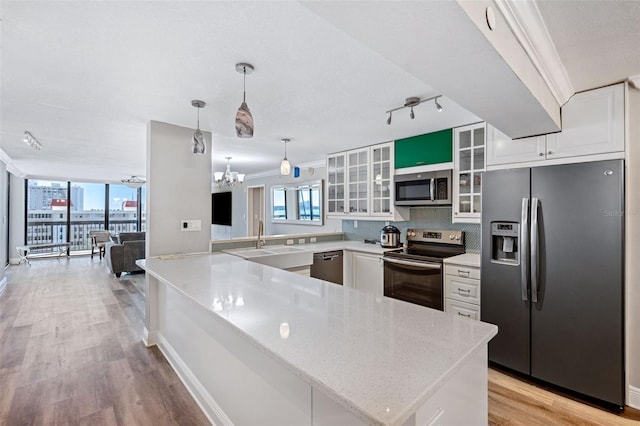 kitchen with appliances with stainless steel finishes, kitchen peninsula, white cabinets, and decorative light fixtures