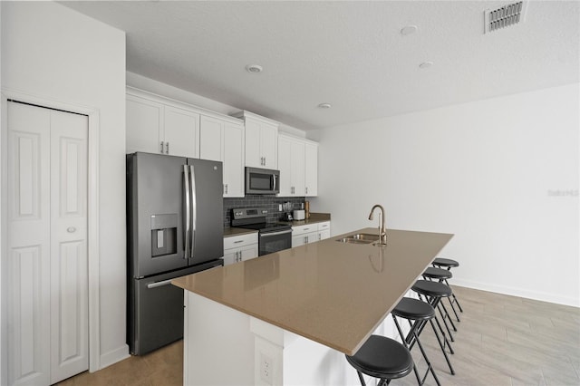 kitchen with white cabinetry, stainless steel appliances, an island with sink, and a breakfast bar area