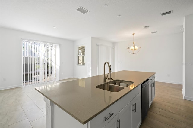 kitchen featuring decorative light fixtures, dishwasher, sink, dark stone counters, and a kitchen island with sink