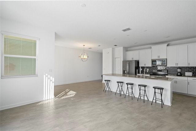 kitchen with appliances with stainless steel finishes, a kitchen bar, decorative backsplash, and white cabinets