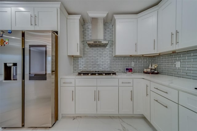 kitchen featuring wall chimney exhaust hood, white cabinetry, tasteful backsplash, light stone counters, and stainless steel appliances