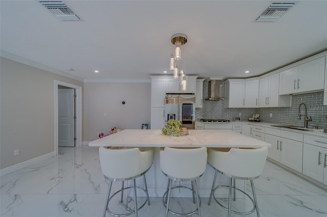 kitchen with stainless steel refrigerator with ice dispenser, sink, decorative light fixtures, a center island, and wall chimney range hood