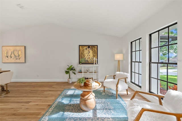 living area with a healthy amount of sunlight, vaulted ceiling, and light hardwood / wood-style flooring