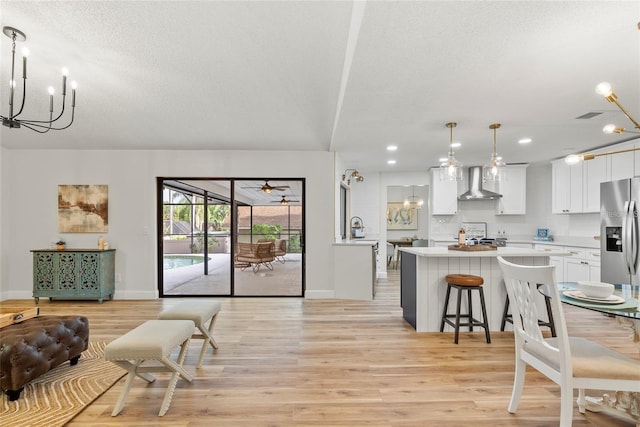 kitchen featuring white cabinetry, light wood-type flooring, stainless steel fridge, pendant lighting, and wall chimney range hood