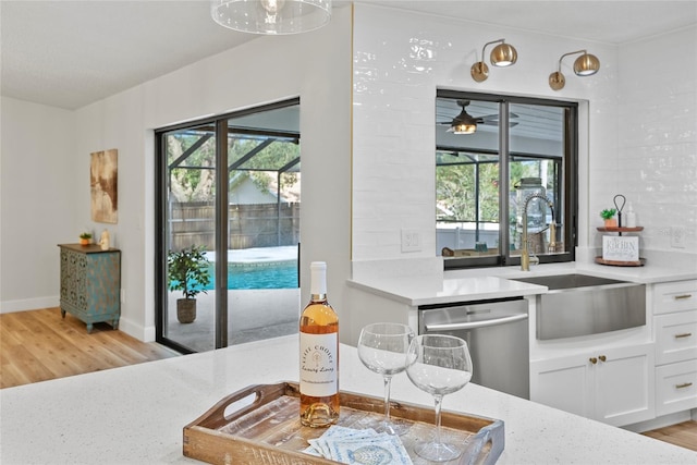 kitchen with white cabinetry, sink, stainless steel dishwasher, and light hardwood / wood-style flooring