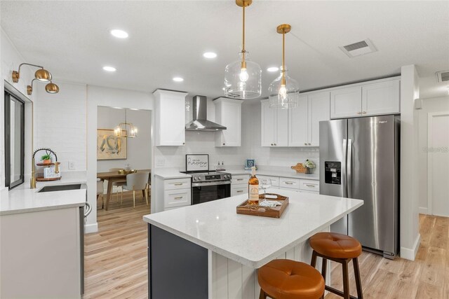 kitchen with pendant lighting, white cabinets, appliances with stainless steel finishes, and wall chimney range hood