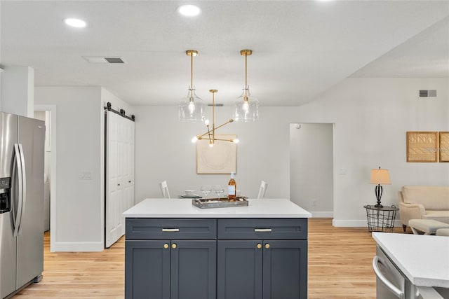 kitchen with a kitchen island, hanging light fixtures, stainless steel appliances, a barn door, and light wood-type flooring