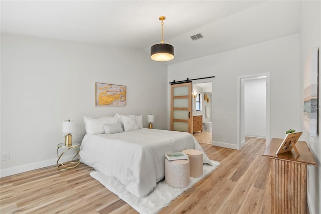 bedroom with vaulted ceiling, a barn door, ensuite bathroom, and light hardwood / wood-style floors