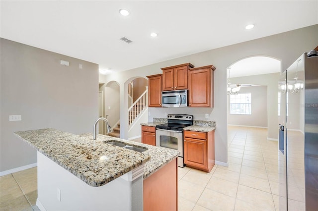 kitchen with sink, light stone counters, light tile patterned floors, appliances with stainless steel finishes, and an island with sink