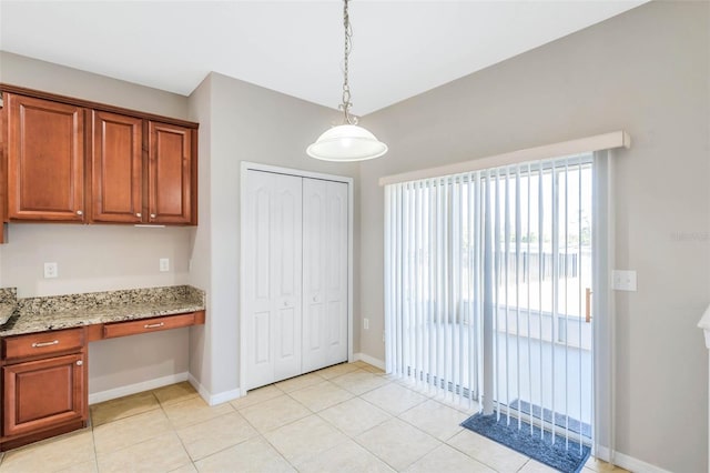 kitchen featuring light tile patterned floors, decorative light fixtures, built in desk, and light stone countertops