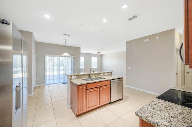 kitchen featuring pendant lighting, an island with sink, sink, stainless steel appliances, and light stone countertops