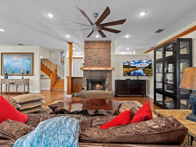 living room featuring ceiling fan, a brick fireplace, a textured ceiling, and light wood-type flooring