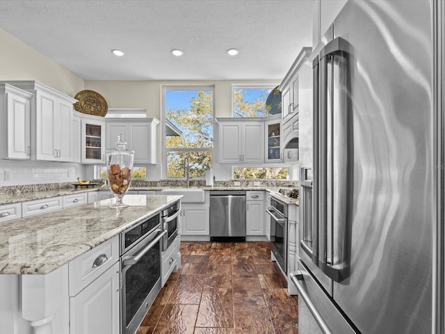 kitchen with appliances with stainless steel finishes, white cabinetry, sink, backsplash, and light stone countertops