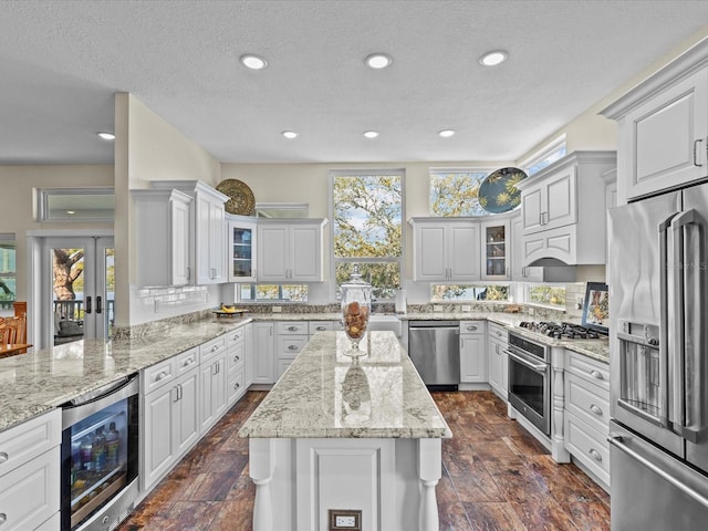 kitchen featuring a kitchen island, appliances with stainless steel finishes, wine cooler, white cabinets, and light stone counters