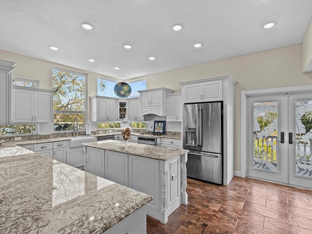 kitchen with french doors, sink, light stone counters, a center island, and high quality fridge