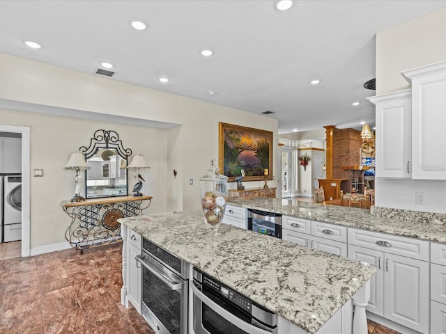 kitchen with a center island, white cabinets, washer / clothes dryer, beverage cooler, and stainless steel oven