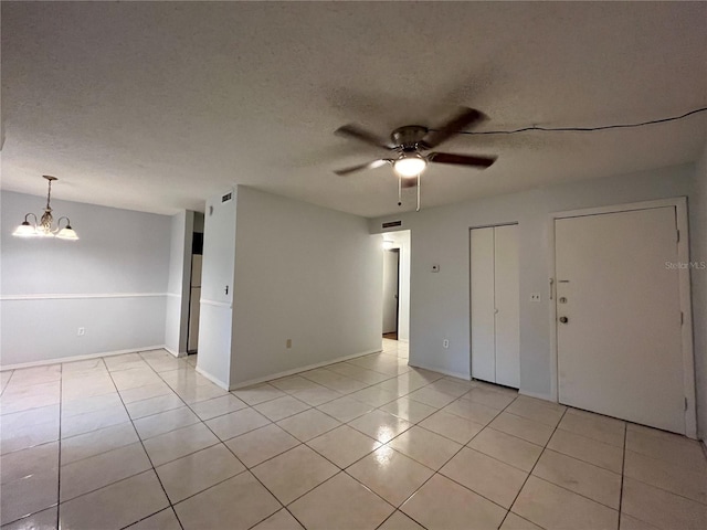 spare room featuring ceiling fan with notable chandelier, a textured ceiling, and light tile patterned floors