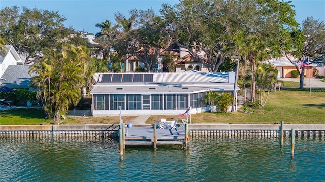 rear view of house featuring a water view, a sunroom, and a lawn