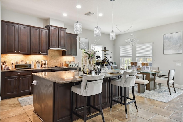 kitchen with a kitchen island with sink, pendant lighting, backsplash, and dark brown cabinetry