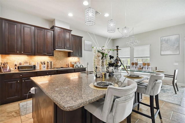 kitchen featuring a kitchen island with sink, pendant lighting, light stone countertops, and a kitchen bar