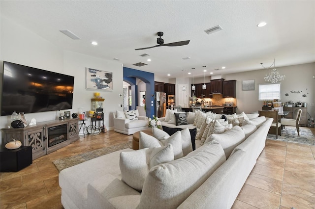 living room featuring ceiling fan with notable chandelier and a textured ceiling