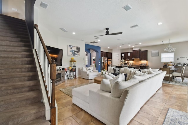 living room featuring ceiling fan with notable chandelier, a textured ceiling, and light tile patterned floors