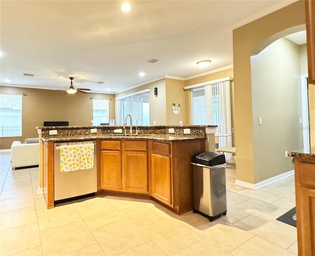 kitchen with sink, dark stone countertops, ornamental molding, dishwasher, and an island with sink