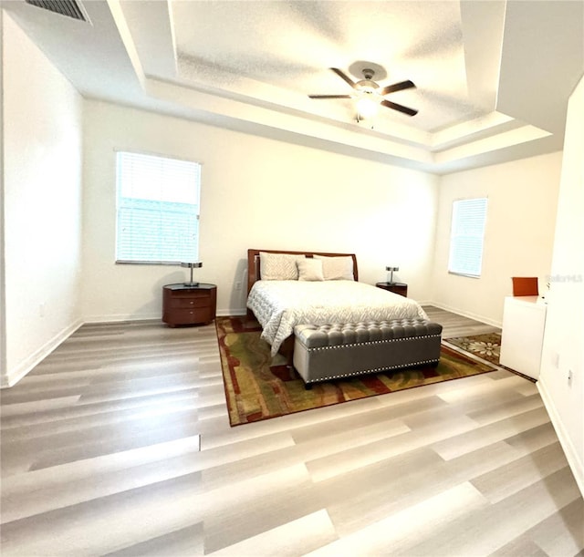 bedroom featuring a raised ceiling, hardwood / wood-style floors, and multiple windows