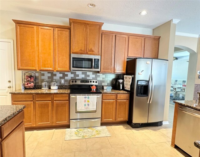 4110 Huntingdale Ct, Wesley Chapel, FL 33543 - kitchen featuring stainless steel appliances, arched walkways, stone counters, brown cabinetry, and backsplash