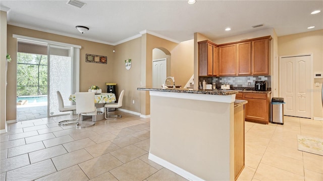 4110 Huntingdale Ct, Wesley Chapel, FL 33543 - kitchen with decorative backsplash, ornamental molding, brown cabinets, arched walkways, and light tile patterned flooring