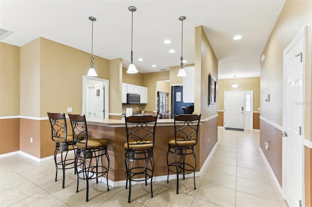 kitchen featuring white cabinetry, light tile patterned floors, a kitchen breakfast bar, and decorative light fixtures