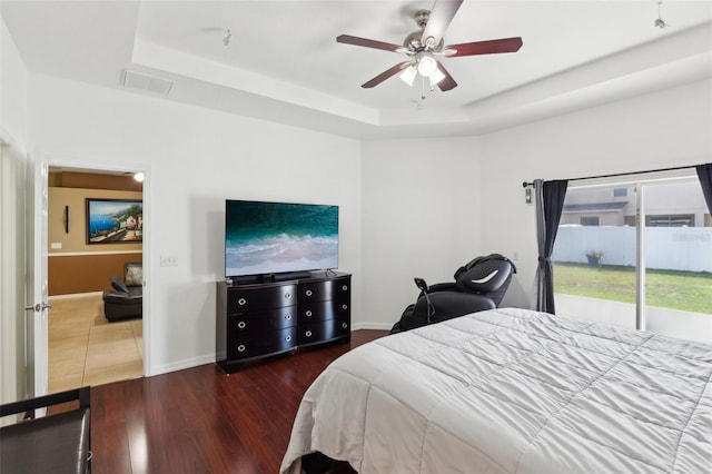 bedroom with dark wood-type flooring, ceiling fan, a tray ceiling, and access to exterior