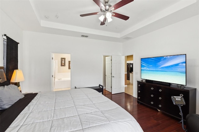 bedroom featuring ceiling fan, hardwood / wood-style floors, ensuite bath, and a tray ceiling