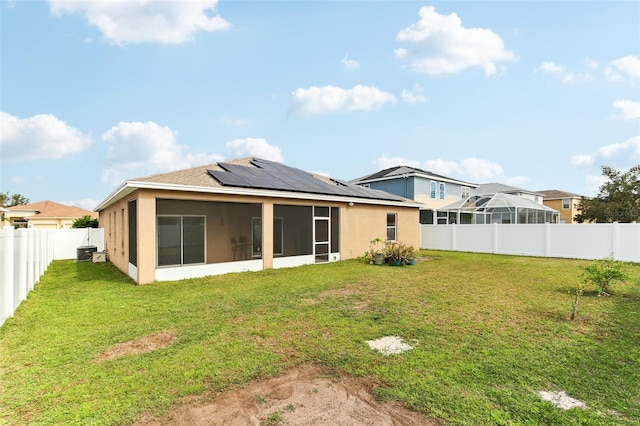 rear view of house featuring a lawn, a sunroom, and solar panels