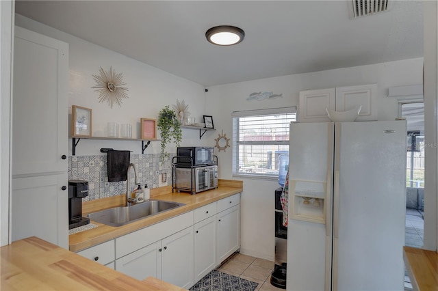 kitchen featuring light tile patterned flooring, butcher block counters, sink, white fridge with ice dispenser, and white cabinets