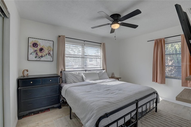 bedroom featuring ceiling fan, a textured ceiling, multiple windows, and light wood-type flooring