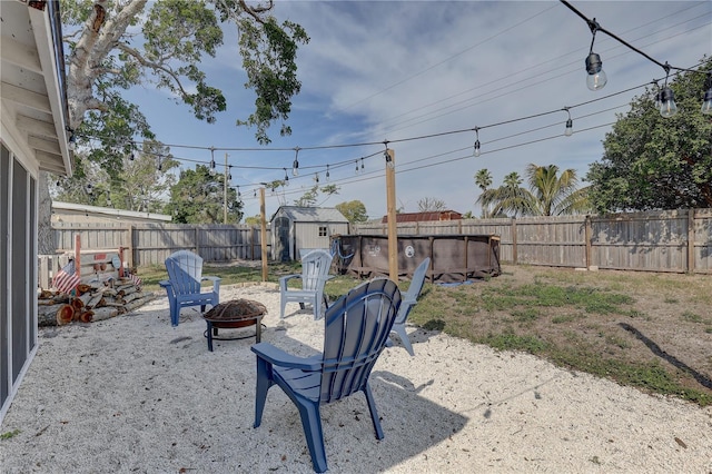 view of yard featuring a storage shed, a fenced backyard, a fire pit, and an outbuilding